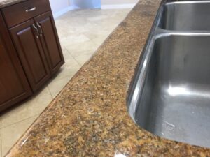 Close-up of a granite countertop with professional repair to a sink rail crack, showcasing seamless color blending and polished finish by Sureshine Care and Restoration Services in Plano, TX.