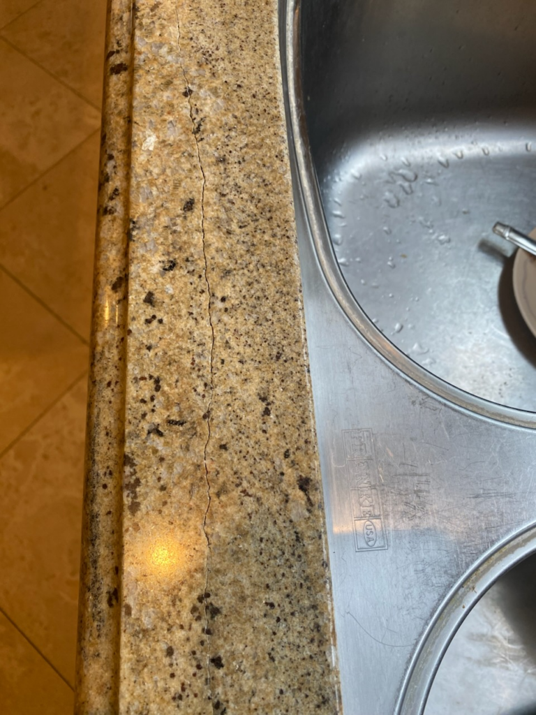 Technician performing granite crack repair on a countertop, using structural stone adhesive and polishing techniques to restore strength and blend the repaired area to match the surrounding granite.