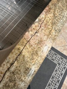 Close-up of a professionally repaired granite countertop crack near a kitchen sink in a Laguna Beach home, fully restored to its original smooth finish.