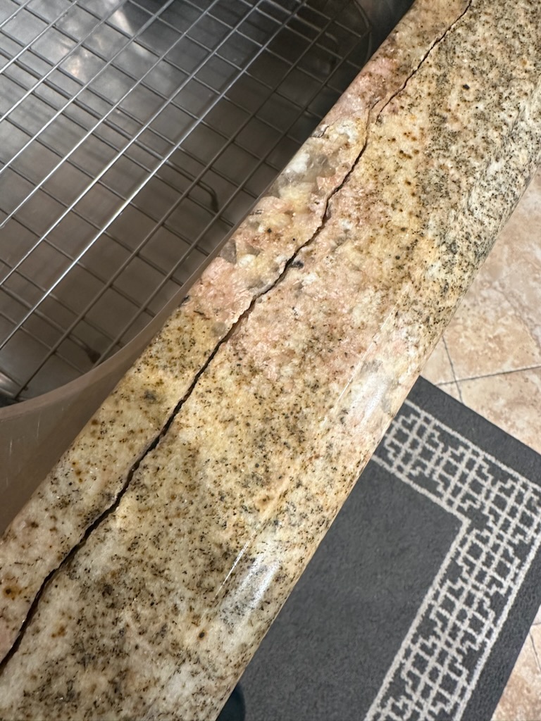 Close-up of a professionally repaired granite countertop crack near a kitchen sink in a Laguna Beach home, fully restored to its original smooth finish.