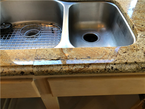 Technician repairing a granite countertop crack near a sink cutout, stabilizing the slab, bonding the crack with stone-grade adhesive, and polishing the surface to match the surrounding finish.