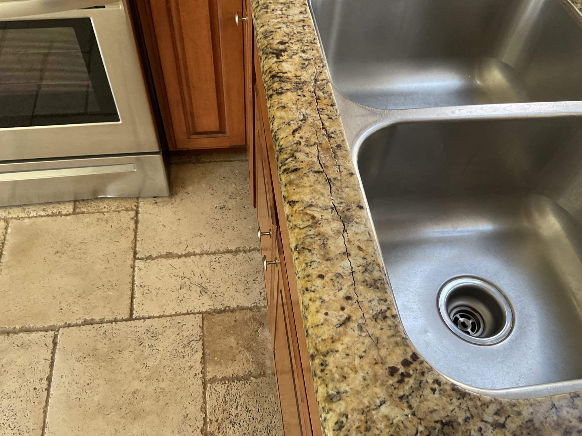 Technician performing granite crack repair on a kitchen countertop, stabilizing and bonding the crack near a sink area to restore strength and create a smooth, blended finish.