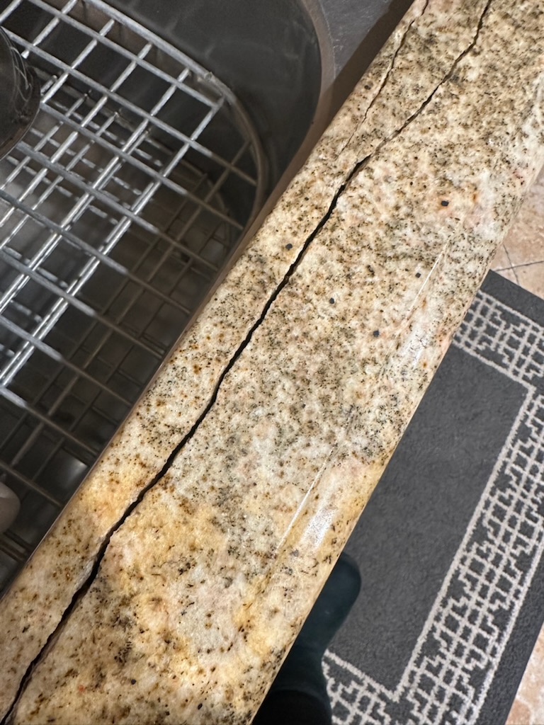 Technician performing granite crack repair on a kitchen island, stabilizing the stone and polishing a bonded crack to blend with the surrounding granite finish.